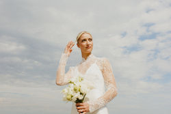 bride brushing hair out of her face with clouds and sky only in the background, moody and editorial