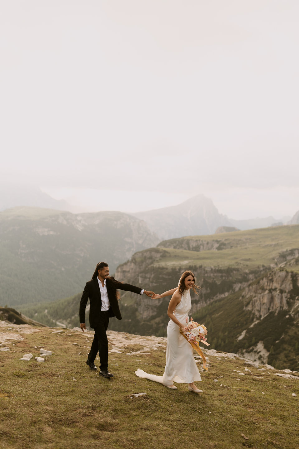 bride and groom walking hand in hand laughing in the Italian dolomites