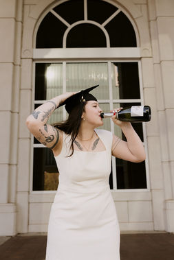 college senior photos on fayetteville campus, graduate is holding her cap as she is drinking champagne to celebrate