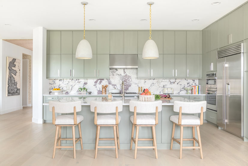 Modern sage olive kitchen with cream bar stools and hanging pendant lights.