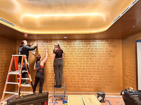Team applying gold-leaf play titles to metallic walls in the Todd Haimes Theatre lobby.