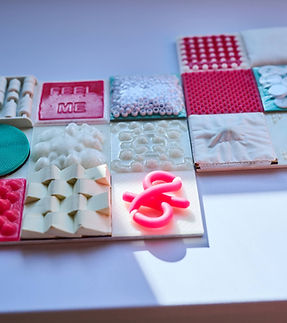 A close-up image of "Look Closer" showing magenta silicone tiles, wooden green tiles, and white tiles with various textures and sensory interactive components.