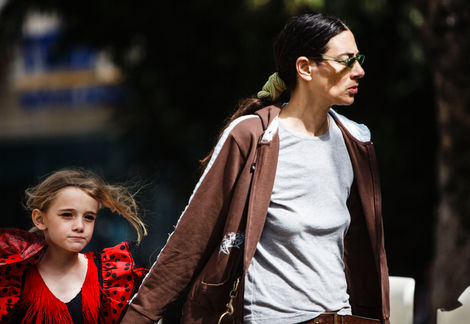 תקריב על אמא וילדה הולכות על המדרכה בתל אביב. האם מחזיקה את הילדה בידה ונראית מעט חסרת סבלנות