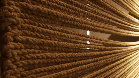 A wall made of horizontal ropes, with light showing from behind