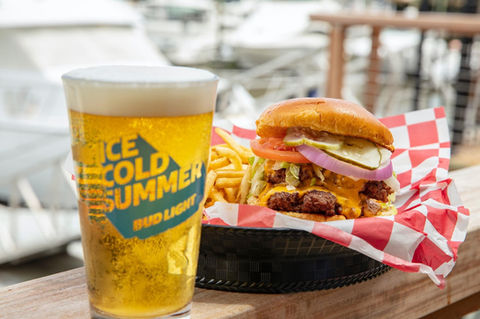 a full beer and a loaded cheesburger with fries in a red and white basket on a table overlooking the marina