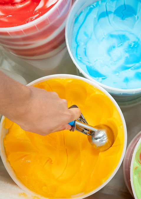 a group of vibrant colored Italian ice tubs with a hand scooping out of the orange tub