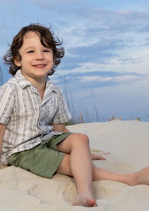 a young boy with brown curly hair poses on the dunes