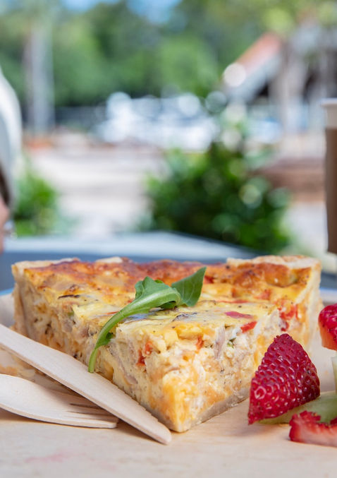 close up of a quiche, strawberries and a coffe cup with the Daily logo and a hand delivering a glass of orange juice