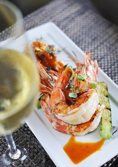large shrimp displayed on a white platter with a glass of white wine