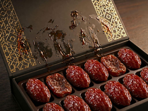 An opened luxury date gift box containing partially flattened dates, with sticky syrup leaked and smeared across the inner lid.