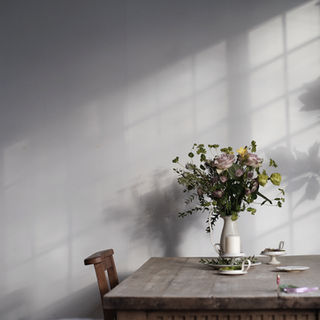 木のテーブルに花と器を配した室内風景。柔らかな自然光が差し込んで美し影をつくっている。