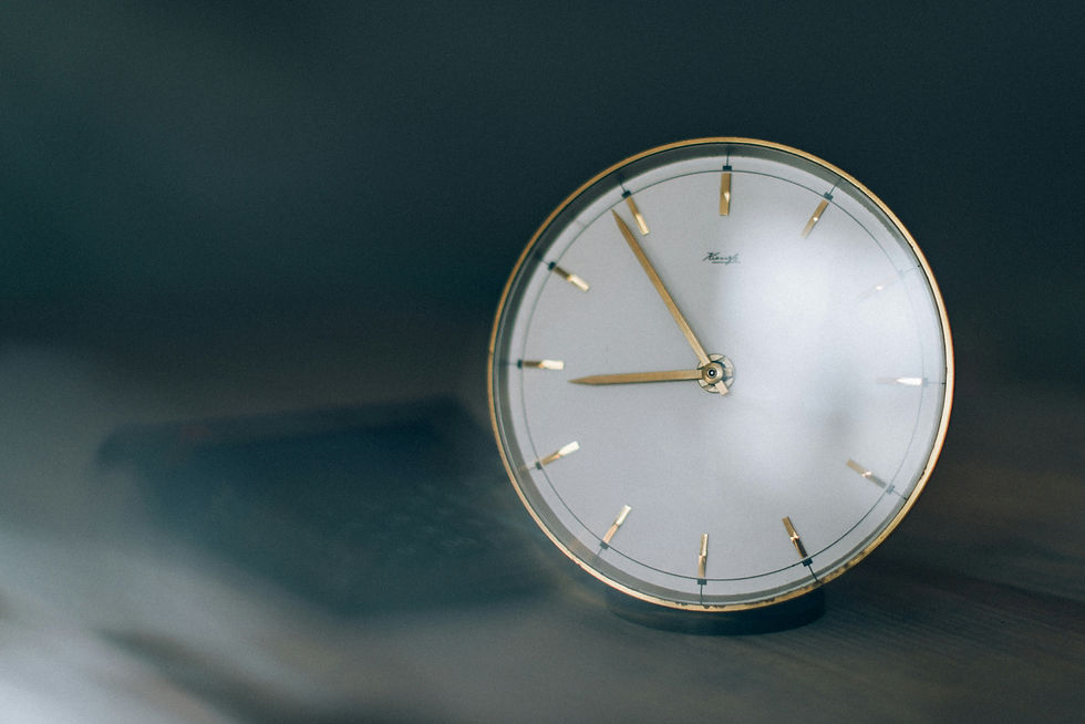 A vintage clock with gold hands and markers on a wooden surface, set against a blurred dark background, exuding a calm, nostalgic mood.