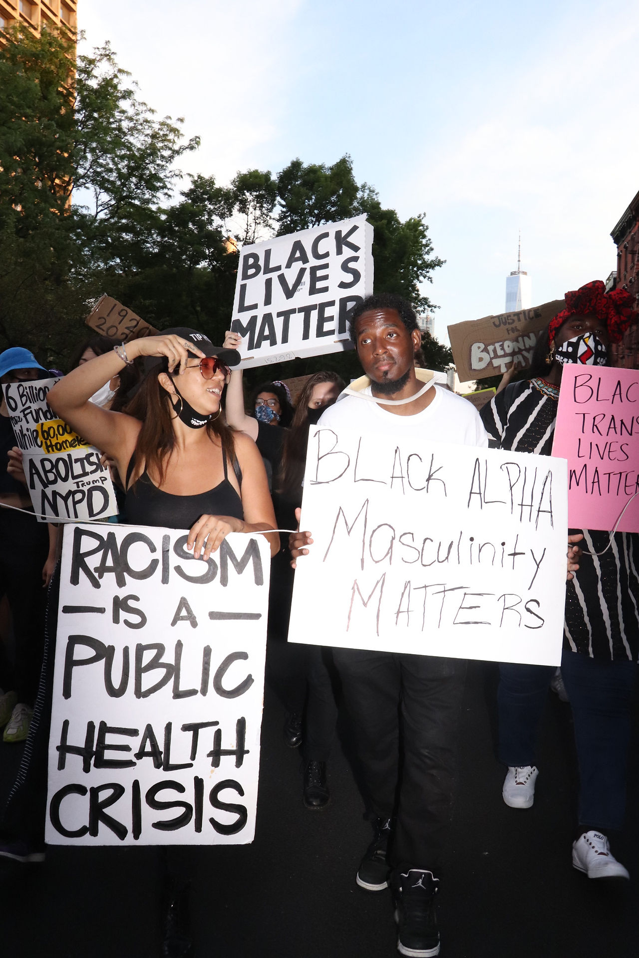 Two protesters march through Greenwich village with signs reading Racism is a Public Health Crisis (left) and Black Alpha Masculinity Matters (right)