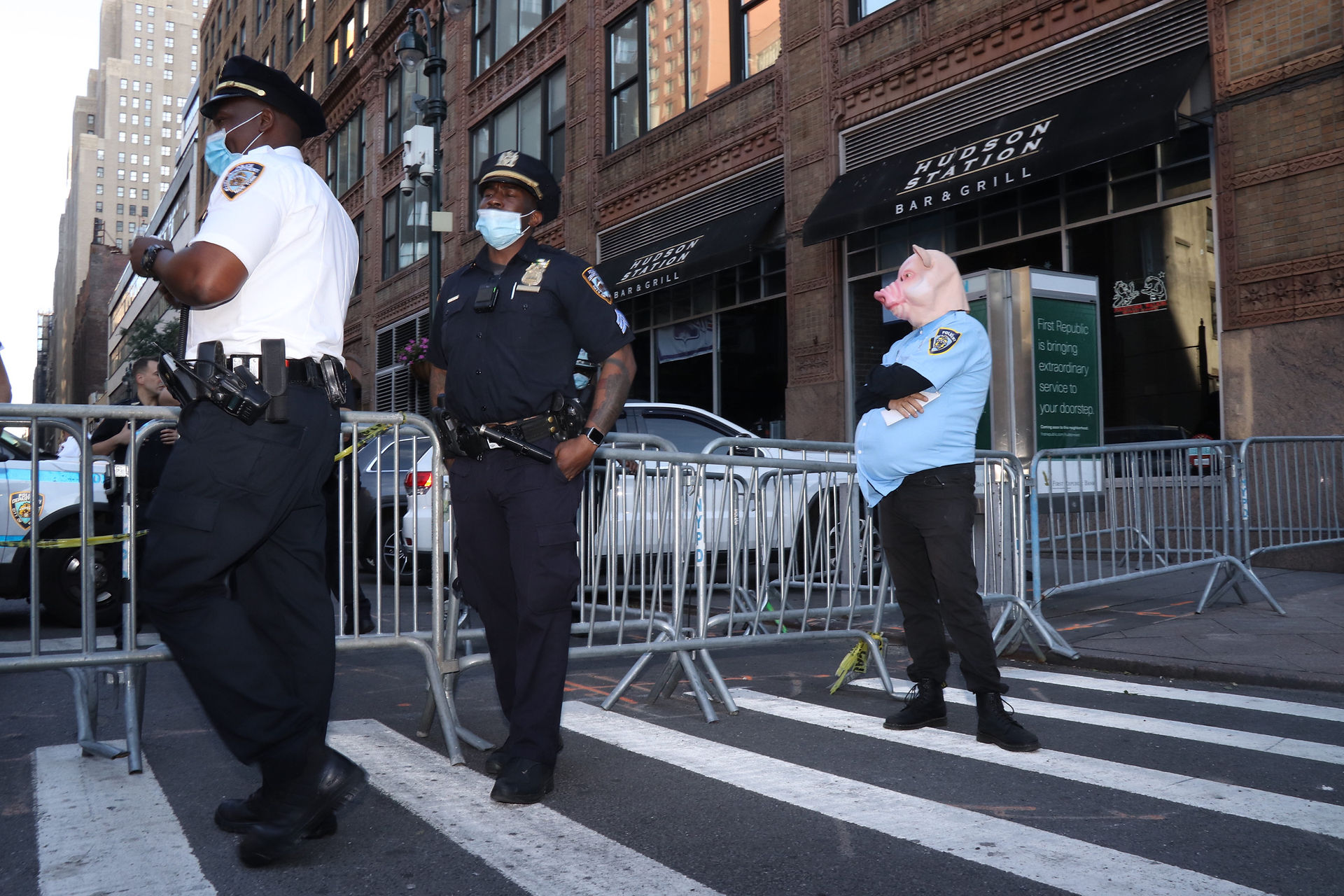 Two police officers (left) and and man dressed as a police officer with a pig mask on (right) observe a march through Hell’s Kitchen