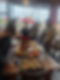 A lively group in a cozy restaurant stands around a table spread with various pastries and dips. Red roses in a vase add a touch of warmth.