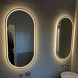 Modern bathroom with two backlit oval mirrors, white vessel sinks, and wall-mounted faucets.