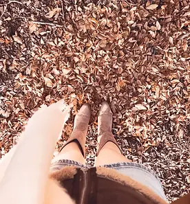 woman dressed for cozy season with brown boots standing in fallen leaves. Cozy romantic autumn book, pumpkin spice romance