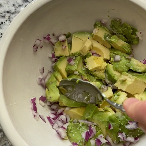 A spoon mashing together avocado, diced red onion, lime juice, and salt