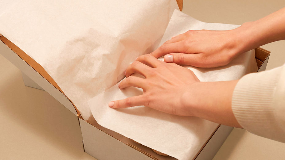 Hands carefully packaging premium footwear with tissue paper in a shoe box