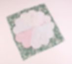 Fabric pieces form a flower shape pinned on a green floral background, displaying pink and white patterns. Light and creative mood.