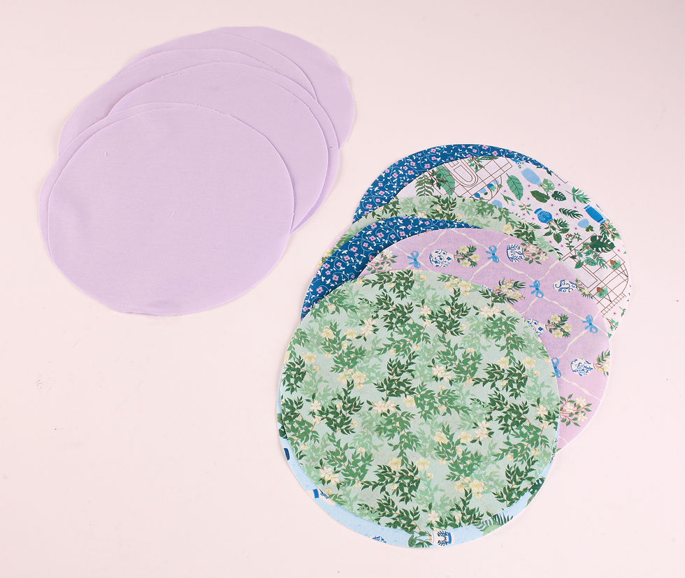 Fabric circles on a light background; some are solid lavender, others have floral and pattern designs in green, blue, and purple.