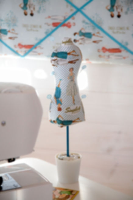 a mannequin shaped pin cushion on a sewing table