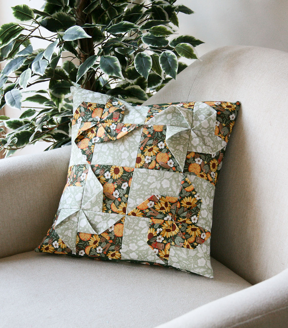 Floral patchwork pillow on beige armchair, green leafy plant in background. Vibrant patterns with white, yellow, and orange flowers. Cozy setting.