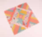 Colorful patchwork quilt square with geometric patterns, florals, and stripes in pink, orange, yellow, and teal on a white background.