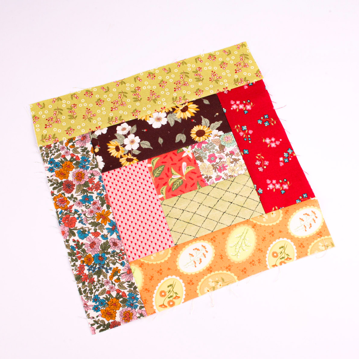 Colorful floral patchwork fabric square on a white background, with red, yellow, pink, and orange patterned squares