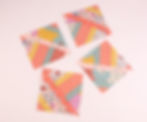 Four colorful quilt squares with floral, chevron, and polka dot patterns on a light pink background.