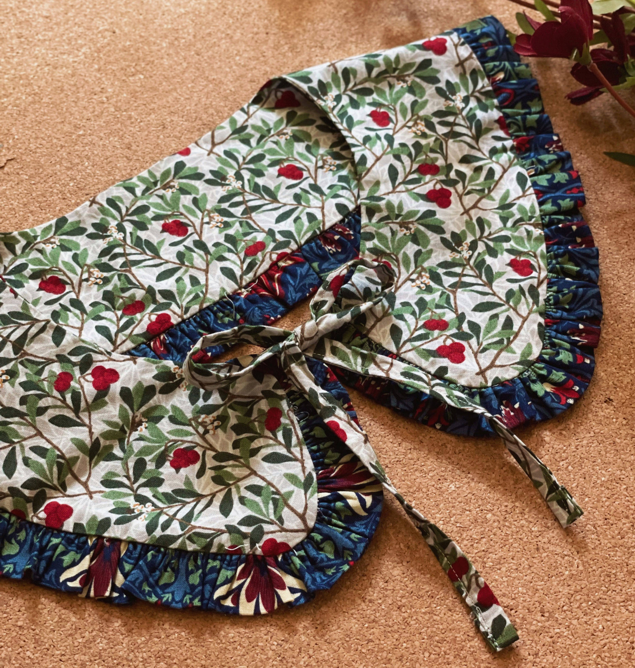 a detachable collar tied with a bow in green and navy floral fabric on a cork background