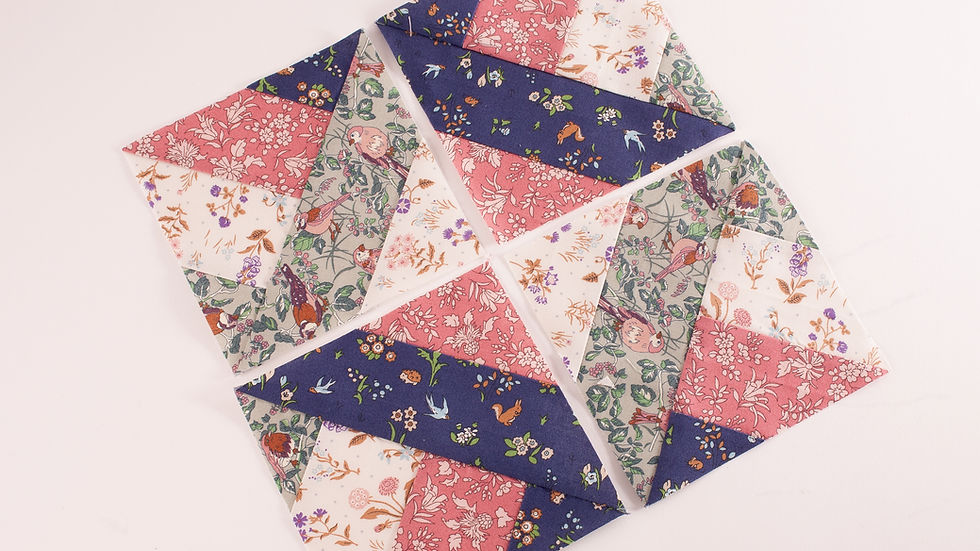 Four patchwork quilt squares with floral patterns in pink, navy, green, and white arranged on a plain white background.