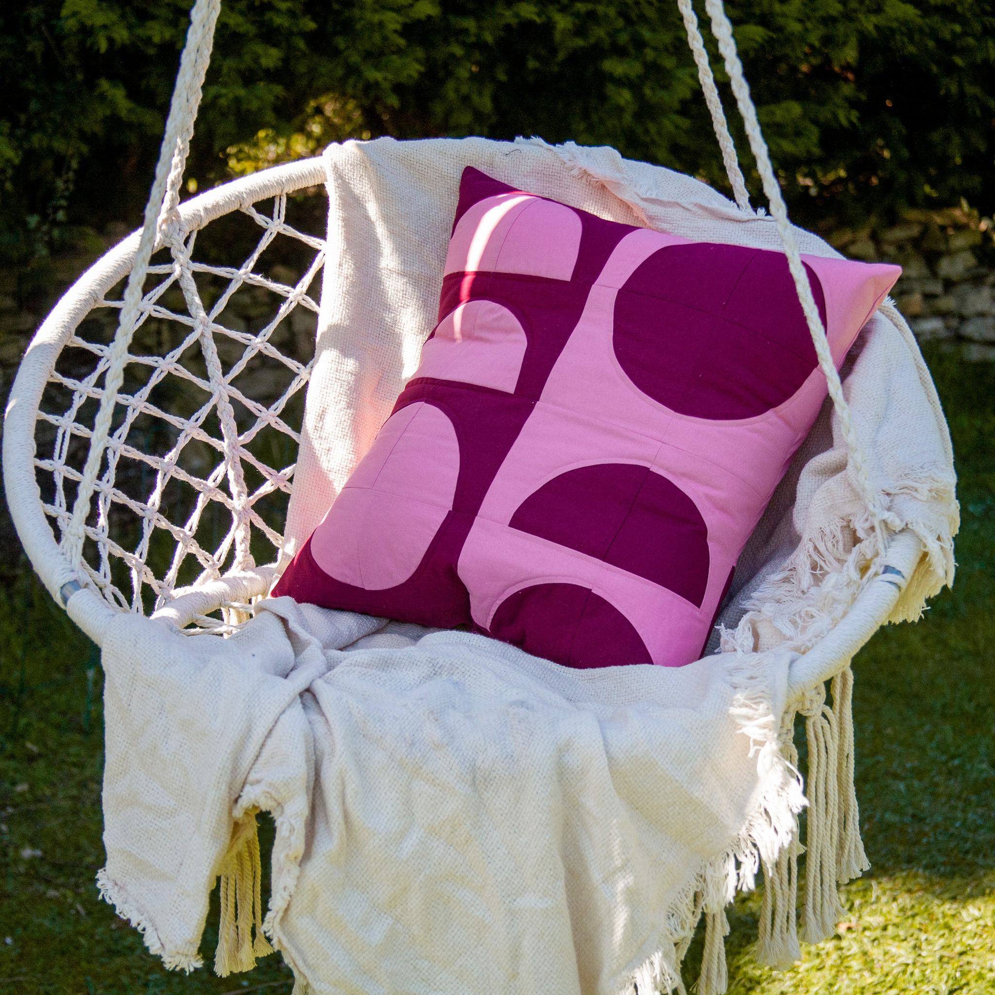 a patchwork cushion cover in pink and burgundy on a crochet swing in a garden