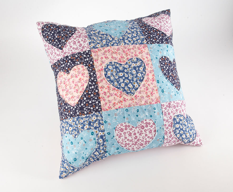 Patchwork pillow with heart patterns in blue, pink, and floral prints on a white background. Cozy and colorful design.