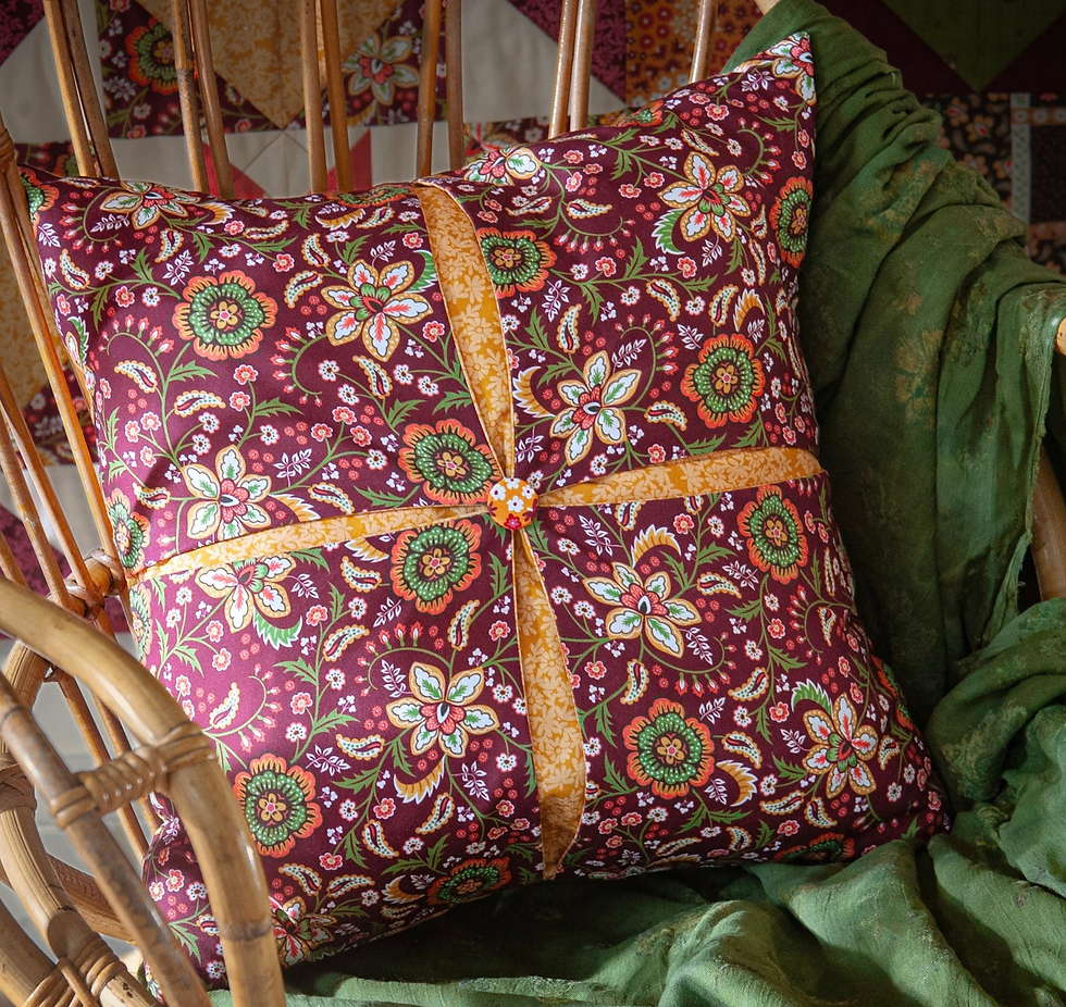 Patterned burgundy floral pillow on a wicker chair, draped with a green blanket, creating a cozy handmade look.