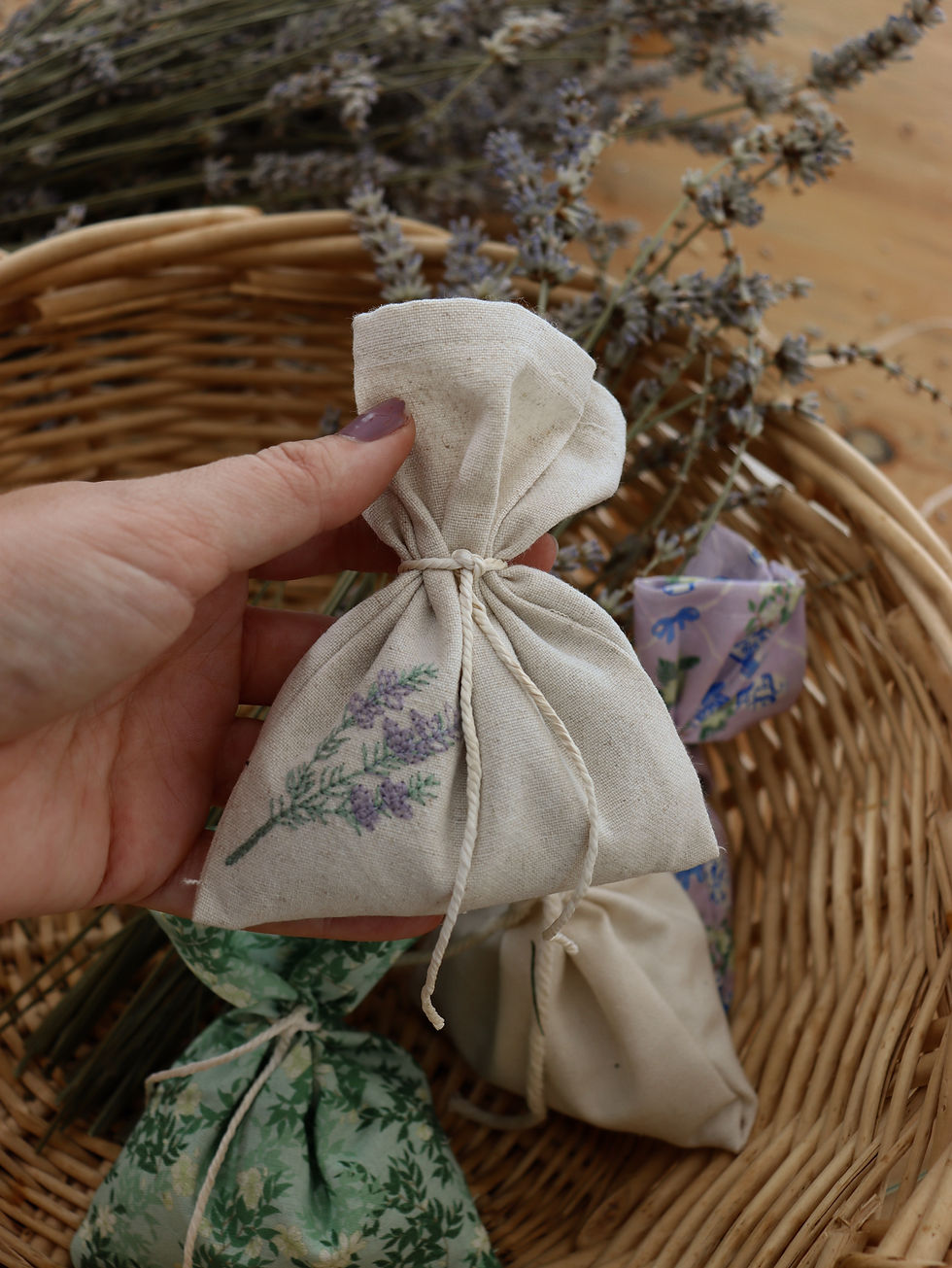 Hand holding a small cloth bag with lavender print, inside a wicker basket with dried lavender stems. Soft, natural colors and calming mood.