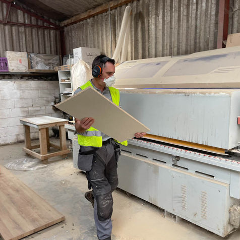Craftsman inspecting wood panel near large machine