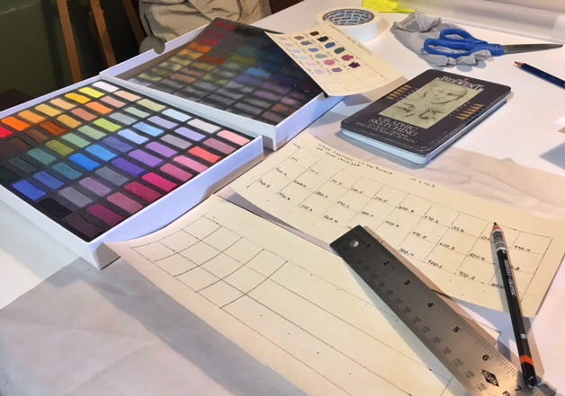 Counter with a box of pastel, ruler, pencils, and swatch chairs in the process of being made.