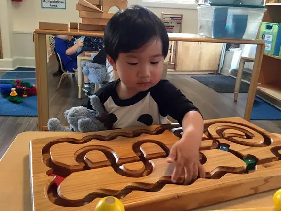 Preschooler concentrating while tracing shapes on a wooden puzzle board