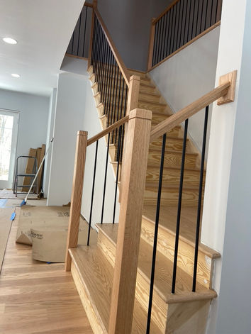 A staircase made of natural wood with black vertical metal bars, complementing a clean and minimalist home design.