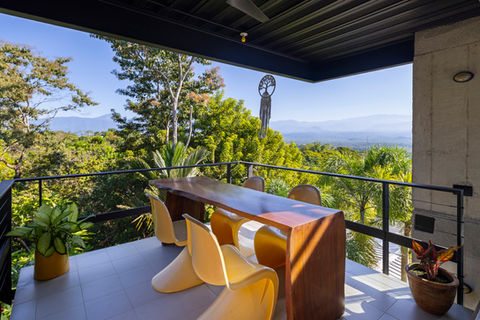 Outdoor dining area at Casa Zenta with a unique wooden table and modern yellow chairs, offering breathtaking views of the lush tropical forest and distant mountains, perfect for enjoying meals surrounded by nature.
