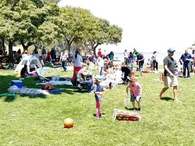 Families and children enjoying outdoor play and picnic during a school-wide park event