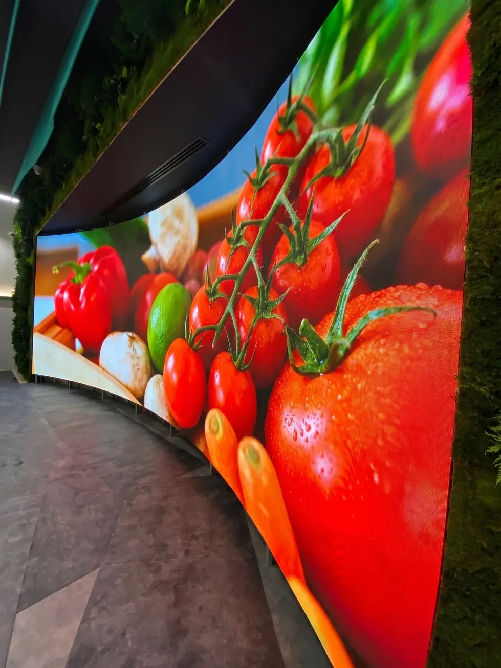Dettaglio ravvicinato e angolato che evidenzia il raggio di curvatura perfetto, l'assenza di fessure tra i cabinet e l'eccezionale fedeltà cromatica del display LED Lamina SR con immagini di pomodori e peperoni.