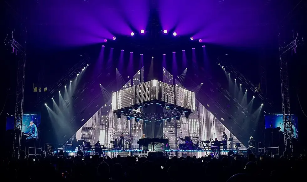 Due inquadrature panoramiche del palasport durante il concerto di Gigi D'Alessio, che mostrano la grandezza del palco a tema urbano e il pubblico sugli spalti.