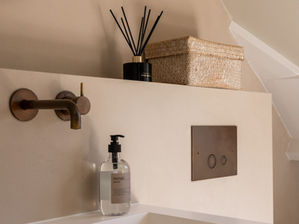 Detail van badkamer met natuurlijke materialen en messing kraan in een lichte ruimte met warme neutrale tinten en rustige uitstraling.