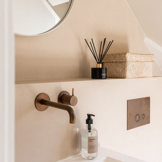 detail van wastafel met bronzen kraan en houten meubel in een badkamer met natuurlijke materialen en warme neutrale kleuren