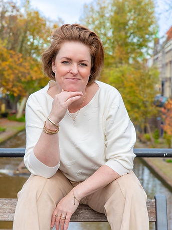 Interieurontwerper Tessa Vermoolen op bankje aan de Oudegracht in Utrecht met herfstkleuren op de achtergrond.
