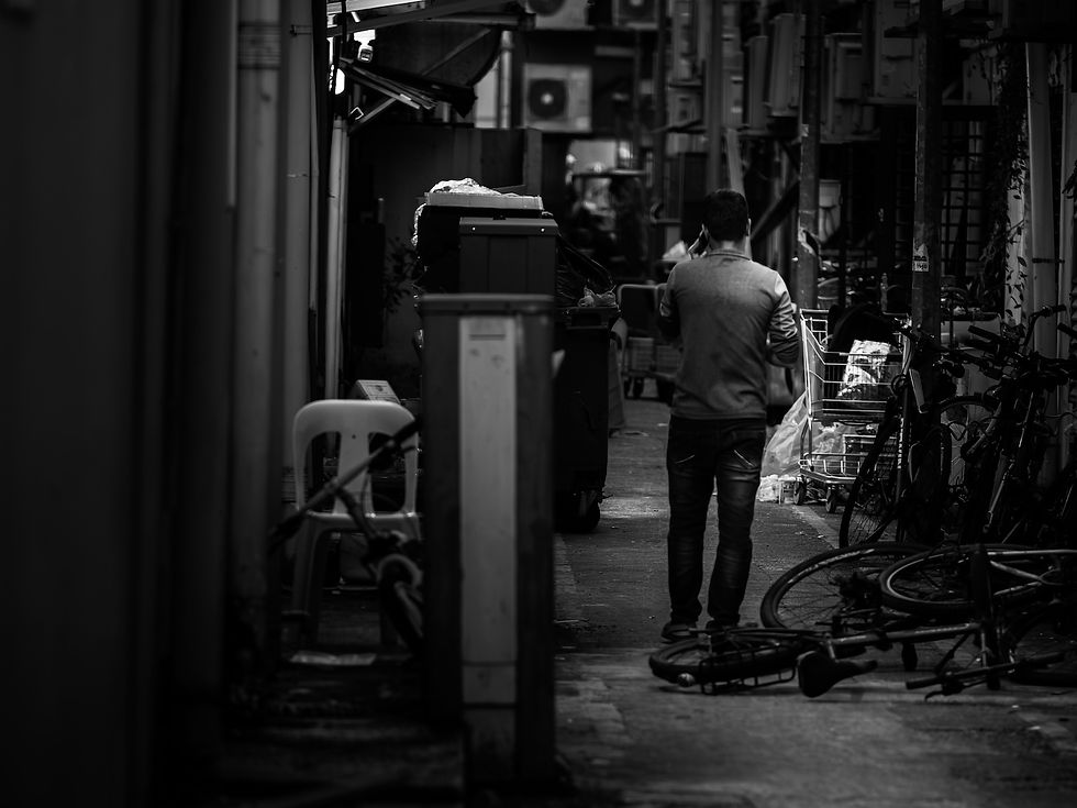 A man walks alone through a narrow alley lined with bicycles, bins, and utility structures in Singapore, photographed in black and white from behind, photographed by Gary PWK for the Made In His Image project.