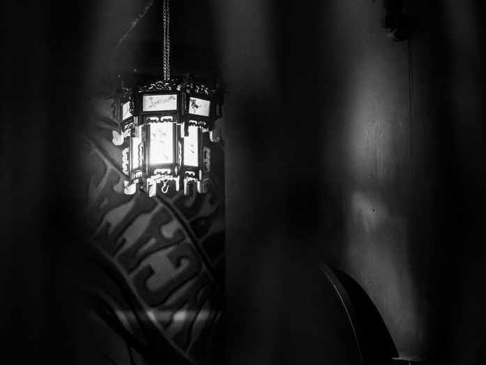 A dimly lit lantern hanging in darkness, casting a small circle of light.
