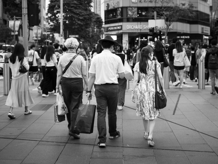 People walking through a crowded crossing area along Orchard Road in Singapore, photographed in black and white with several figures moving in different directions through the city walkway, photographed by Gary PWK for the Made In His Image project.